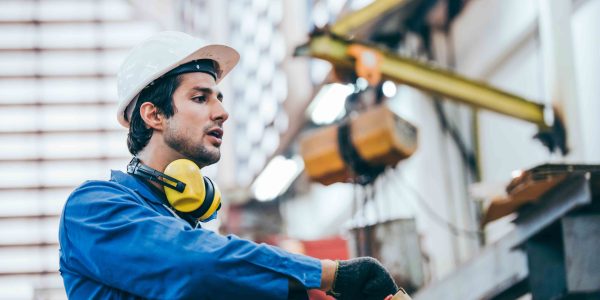 Caucasian mechanic engineer man using equipment to control machine in industrial factory. technician male wearing protective hardhat and uniform working in technology invention industry manufacturing